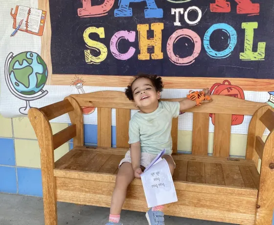 A child sitting on a bench under a colorful Welcome Back to School sign