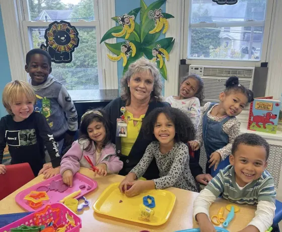A teacher smiling with a group of children working at a classroom table