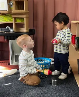 Two toddlers playing in the classroom play kitchen
