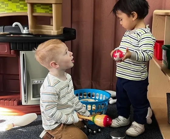 Two toddlers playing together in the classroom play kitchen